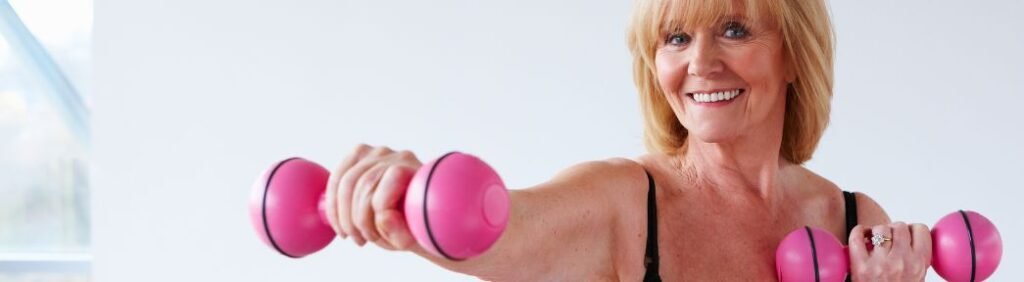 Mulher madura sorrindo enquanto faz exercícios com halteres cor de rosa para manter a massa muscular na menopausa