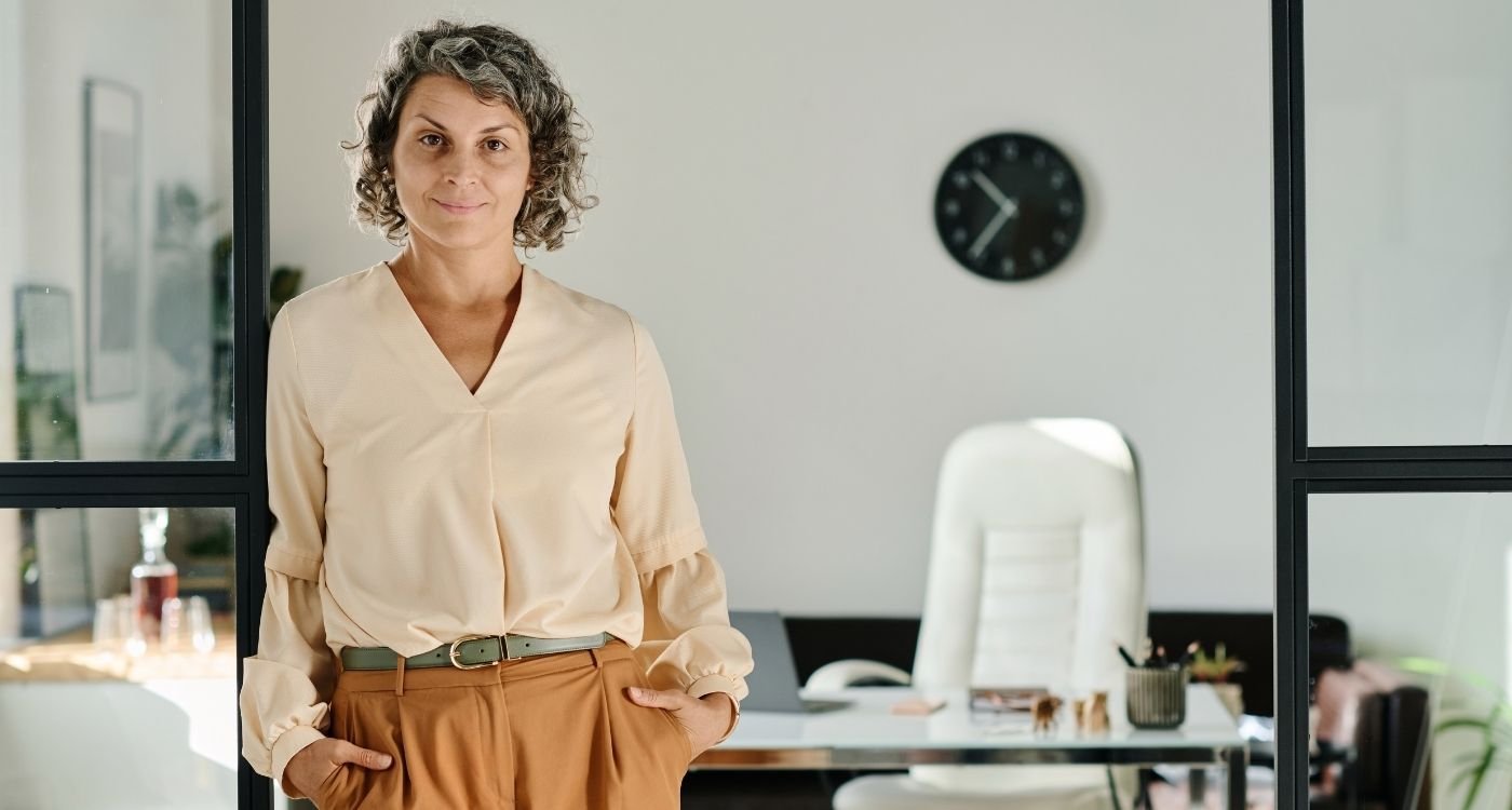 Mulher madura de cabelos grisalhos em ambiente de trabalho, transmitindo confiança e equilíbrio entre climatério e carreira.