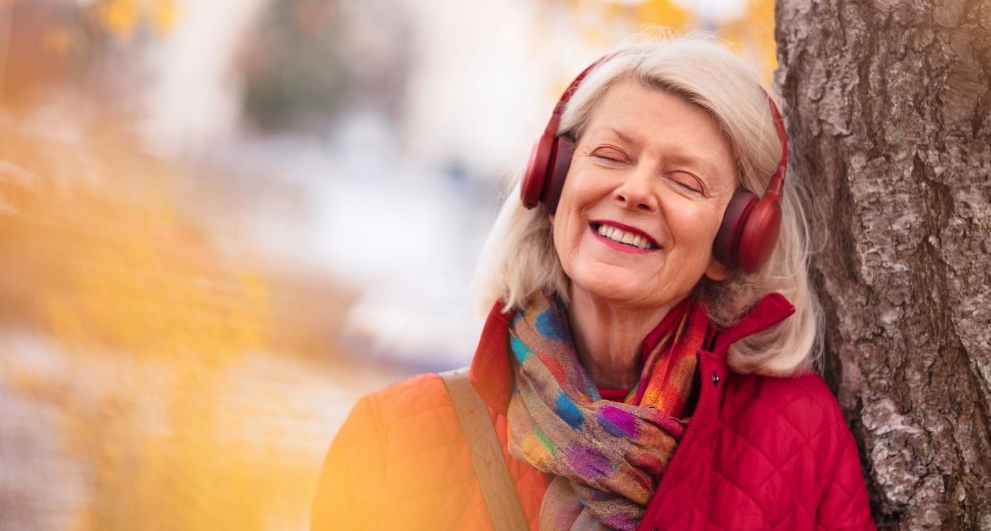 Mulher 50+ sorridente, relaxando com fones de ouvido em ambiente ao ar livre, simbolizando os benefícios da fosfatidilserina na menopausa para memória, foco e bem-estar emocional.