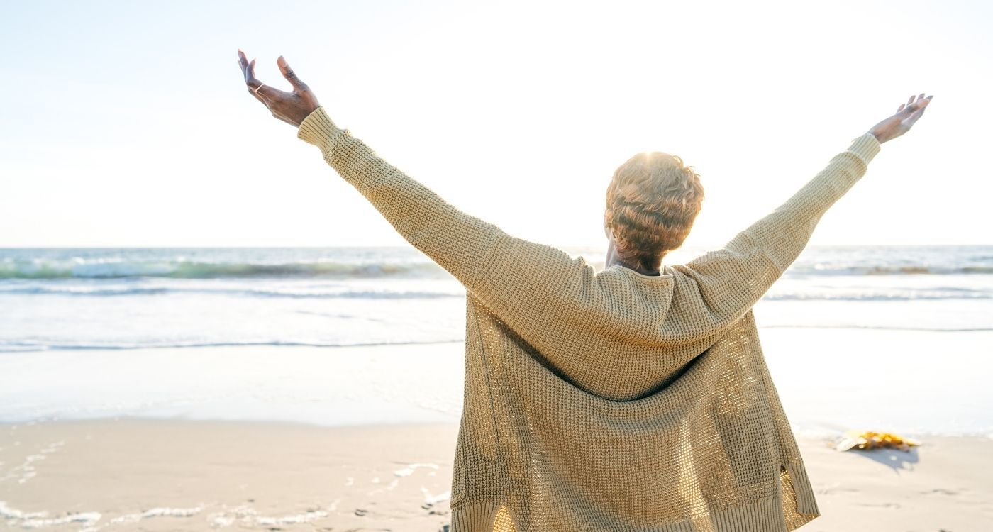 Mulher madura na praia com os braços abertos para o céu — imagem de capa sobre planejamento previdenciário