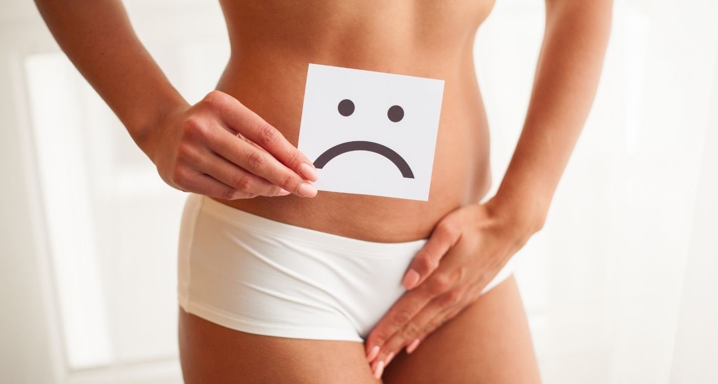 Mulher com calcinha branca cobrindo a região íntima e segurando símbolo de rosto triste, representando corrimento na menopausa.