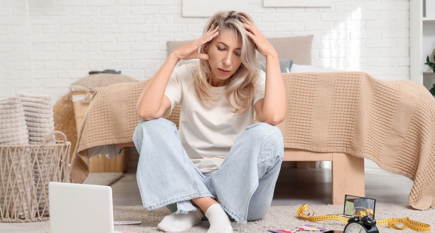 Mulher jovem sentada com expressão preocupada, representando dúvidas e impacto emocional da menopausa precoce.