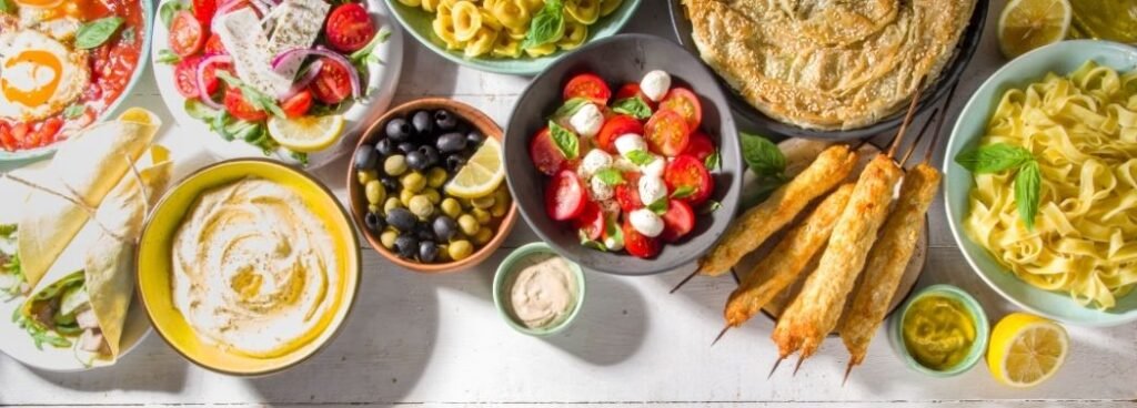 Dieta mediterrânea na menopausa: mesa com saladas, azeite, azeitonas, torta folhada, massas e espetos de frango.