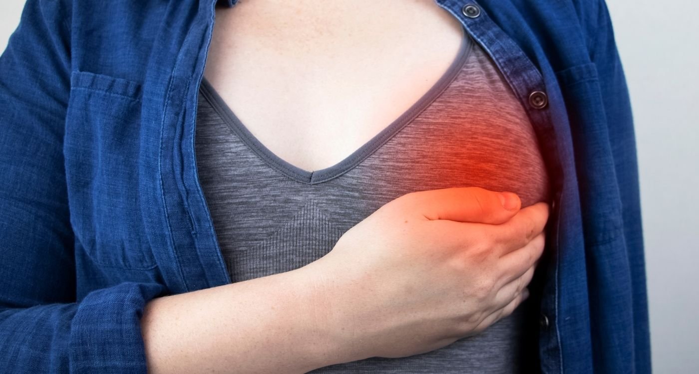 Mão feminina pressionando o seio com leve destaque vermelho, simbolizando dor nas mamas na menopausa.
