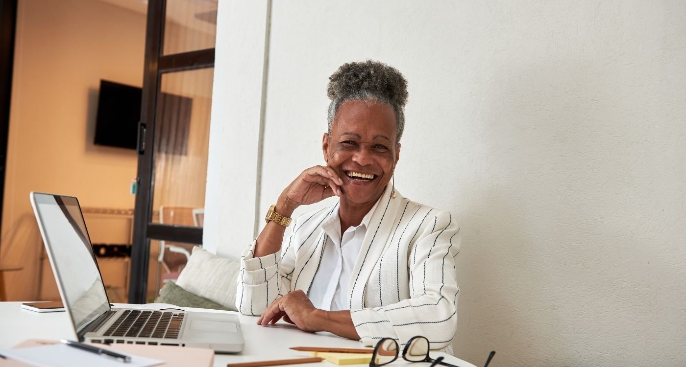 Mulher madura sorridente trabalhando em home office, representando o ato de empreender depois dos 40.