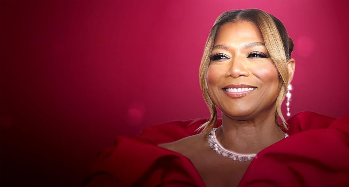 Queen Latifah sorridente em fundo vermelho; notícia sobre Queen Latifah e menopausa