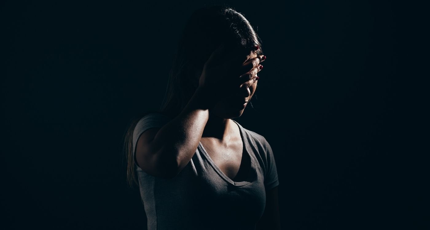 Ansiedade na menopausa: mulher 40+ em fundo escuro, mão cobrindo parte do rosto e expressão tensa, sugerindo preocupação e cansaço.