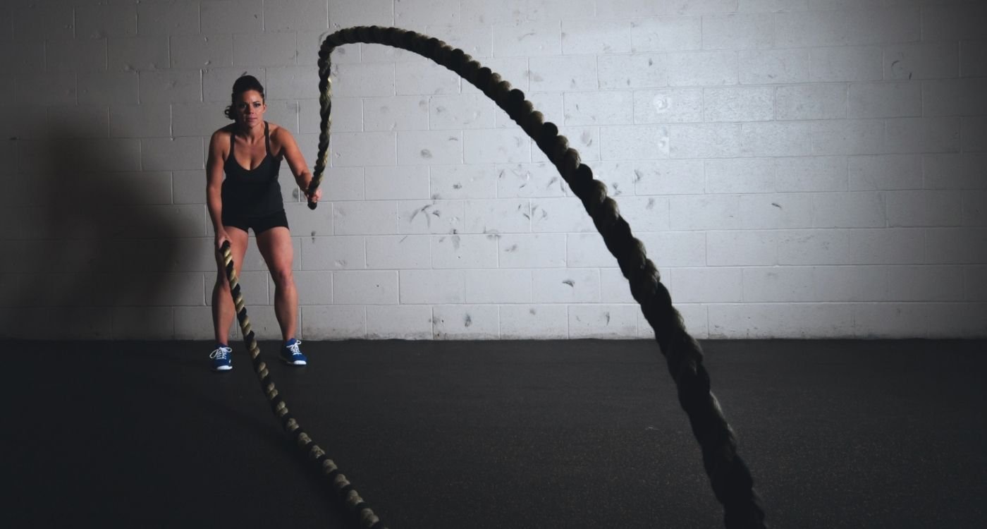 Mulher 40+ treinando com corda naval em academia — musculação na menopausa