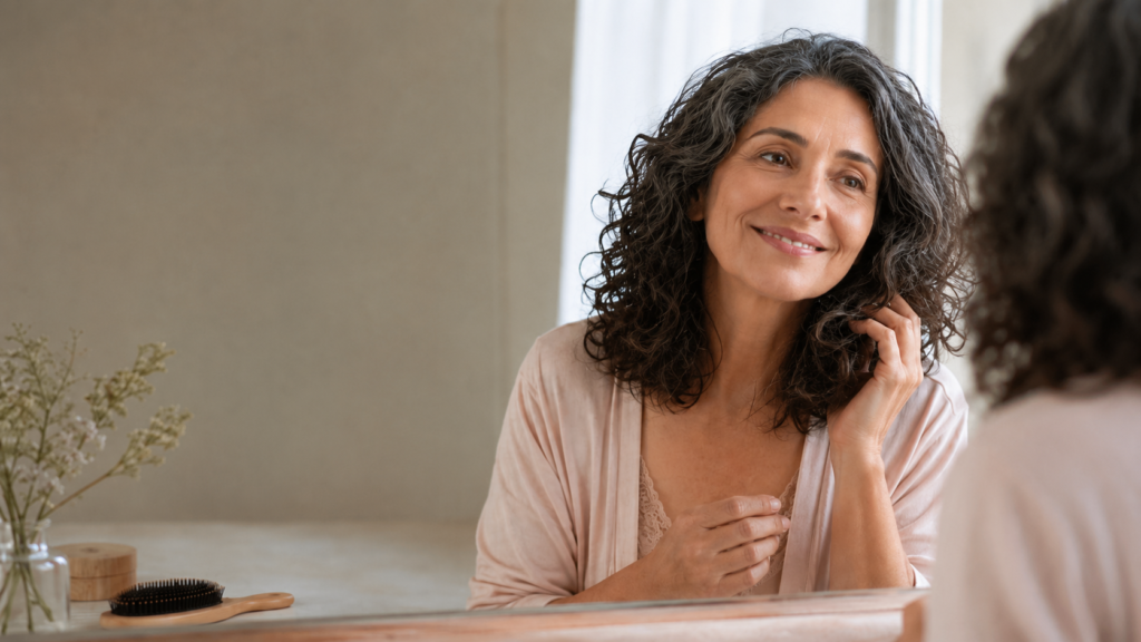 Mulher observa o cabelo ressecado na menopausa diante do espelho.